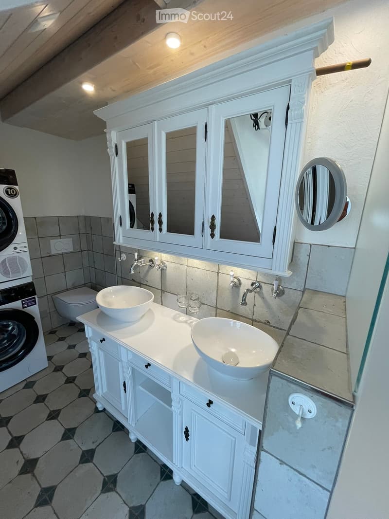 Elegant bathroom with double sink vanity, white cabinets, mirrors, and a washing machine visible in the background.