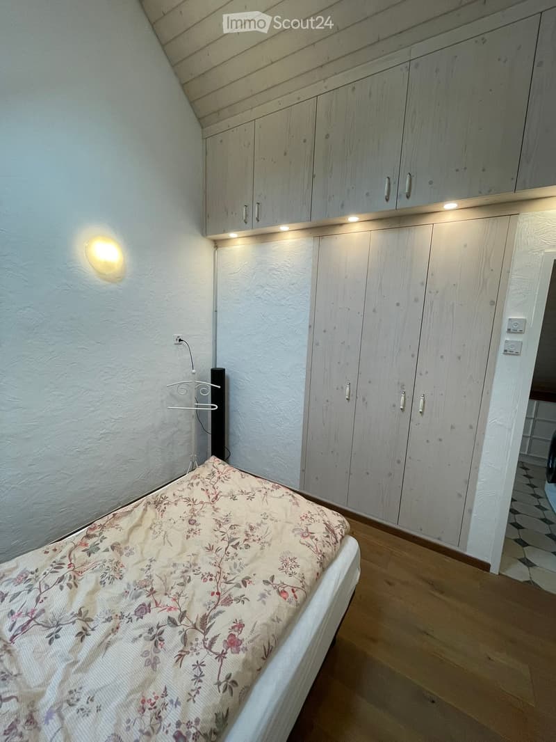 A small bedroom with a single bed, floral bedspread, built-in wardrobes, and warm lighting.