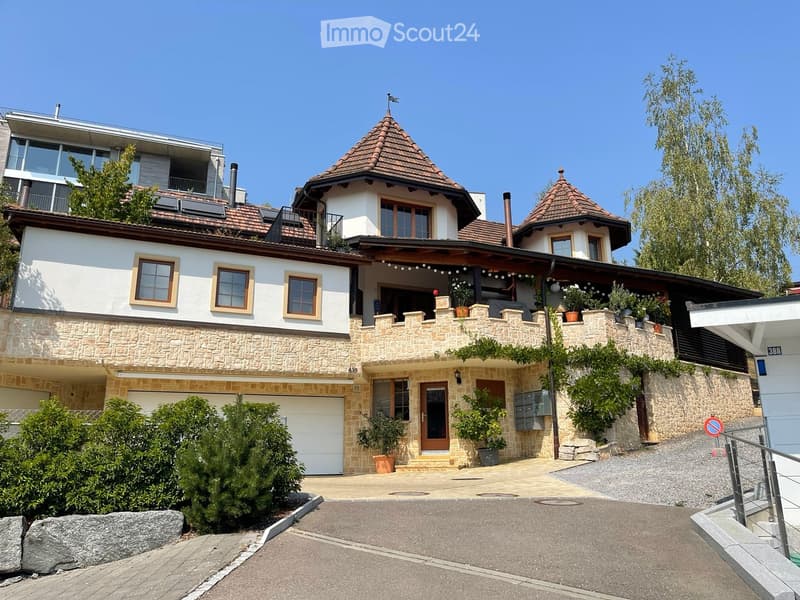 A two-story house with a stone facade, multiple windows, a garage, and a balcony area with potted plants.