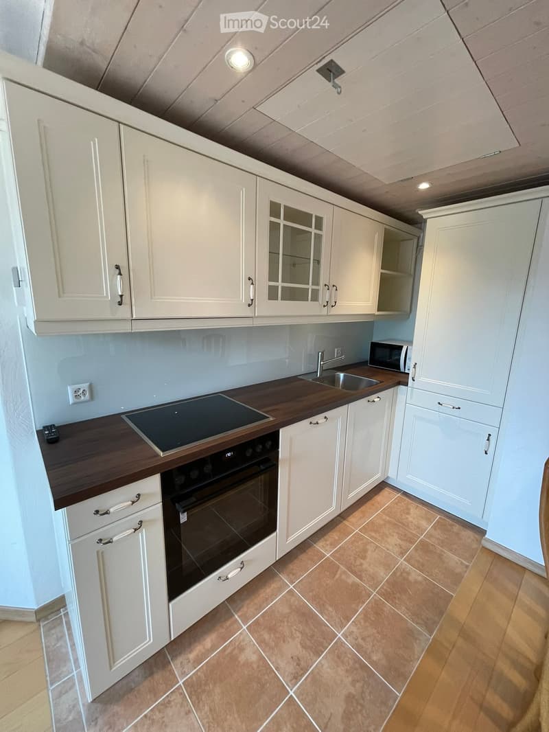 Modern kitchen with white cabinets, wooden countertops, and built-in appliances including an oven, microwave, and induction cooktop.