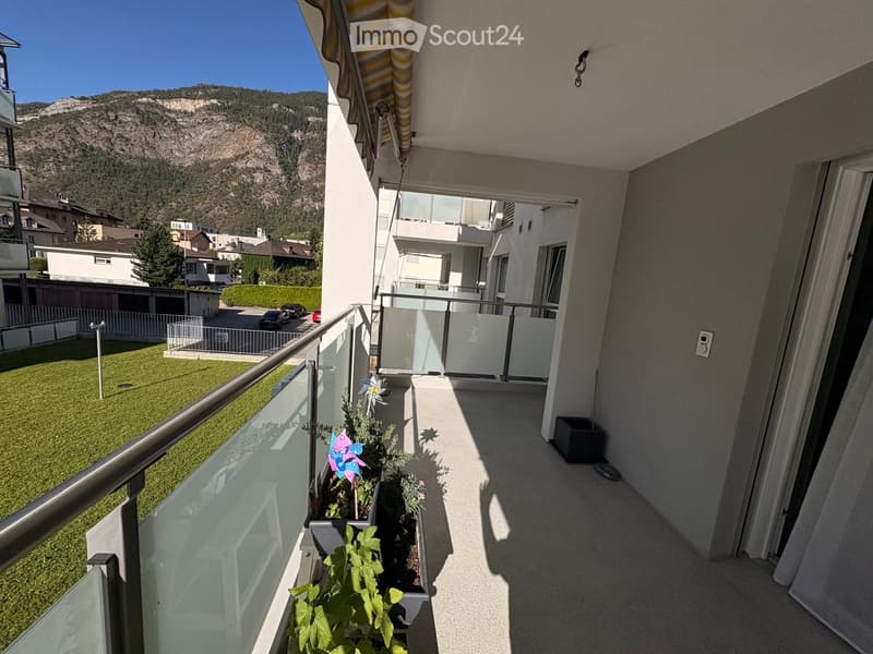 Balcony with a metal railing, potted plants, and a scenic mountain view in the background.