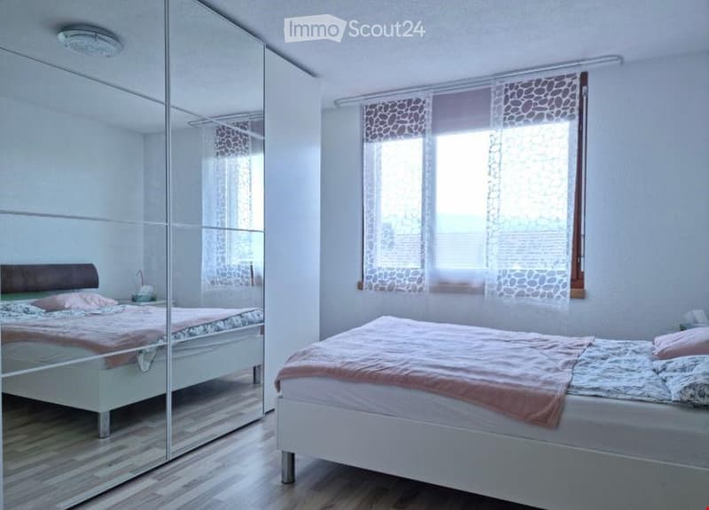 Bright bedroom with two single beds, mirrored wardrobe, wooden flooring, and sheer curtains on the window.