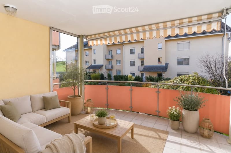 A furnished balcony with a white sofa, wooden coffee table, potted plants, and decorative items.