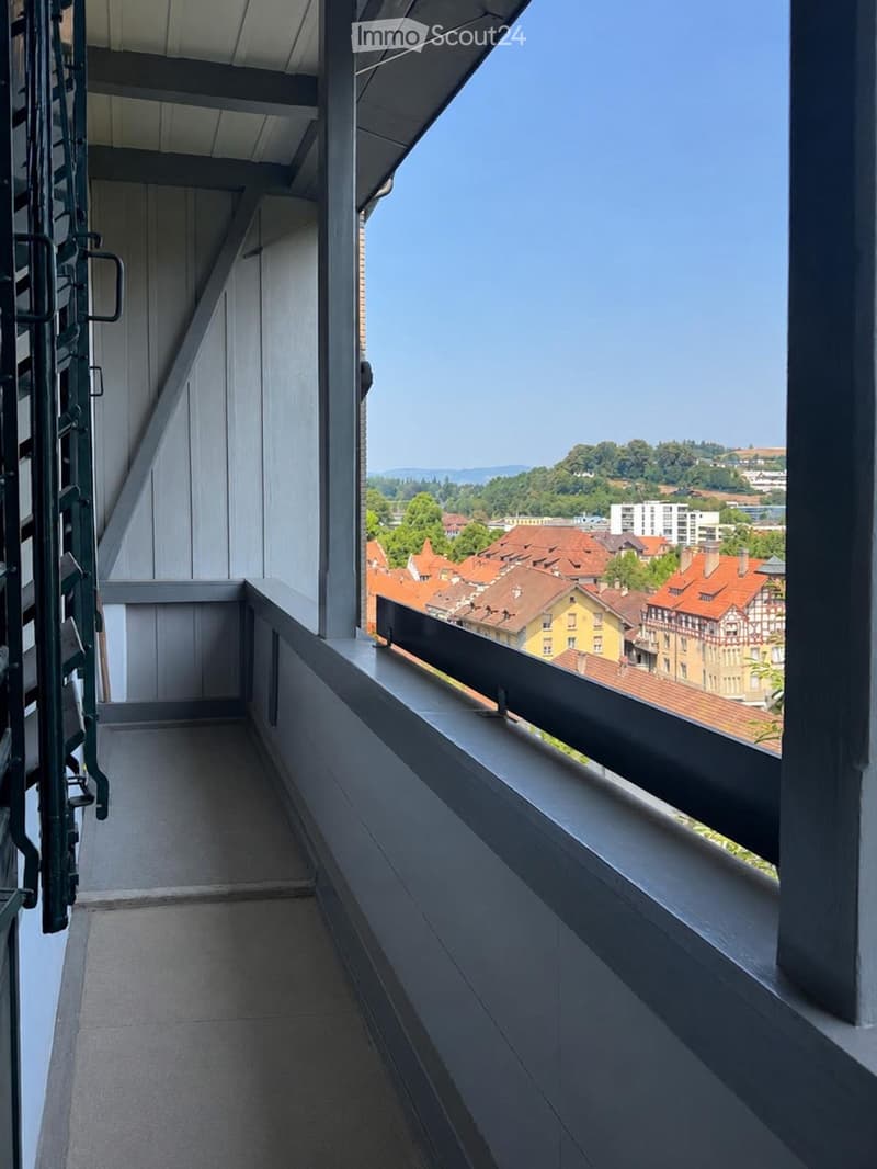 Balcony with a view of a town with red-roofed buildings and distant hills.