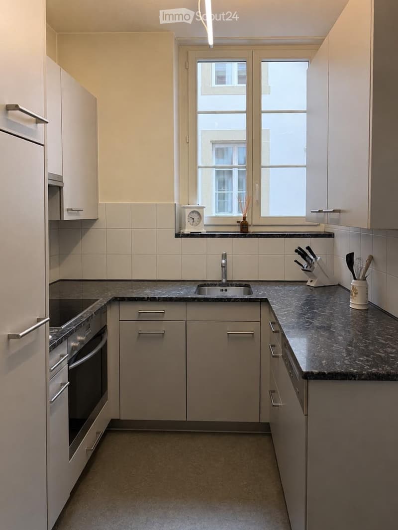 Modern kitchen with light-colored cabinets, granite countertops, stainless steel sink and oven, and various kitchen accessories.