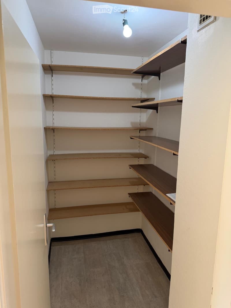 Empty closet with wooden shelves and a single light fixture, featuring a tiled floor and white walls.