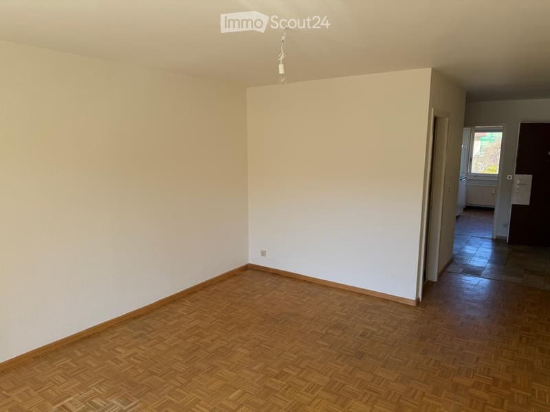 Empty room with wooden parquet flooring and white walls, featuring a visible light fixture and an open doorway leading to another tiled area.