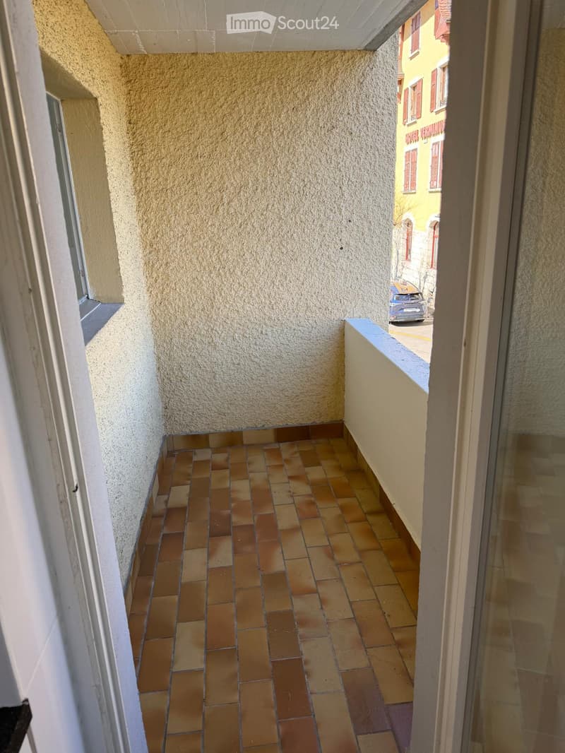Balcony with tiled floor, beige walls, and a view of a neighboring building and street.