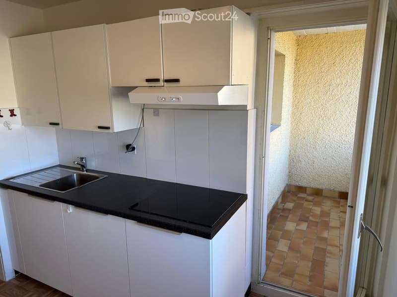 Modern kitchen with white cabinets, black countertop, stainless steel sink, and range hood. The floor is tiled, and there is a doorway leading to another room.
