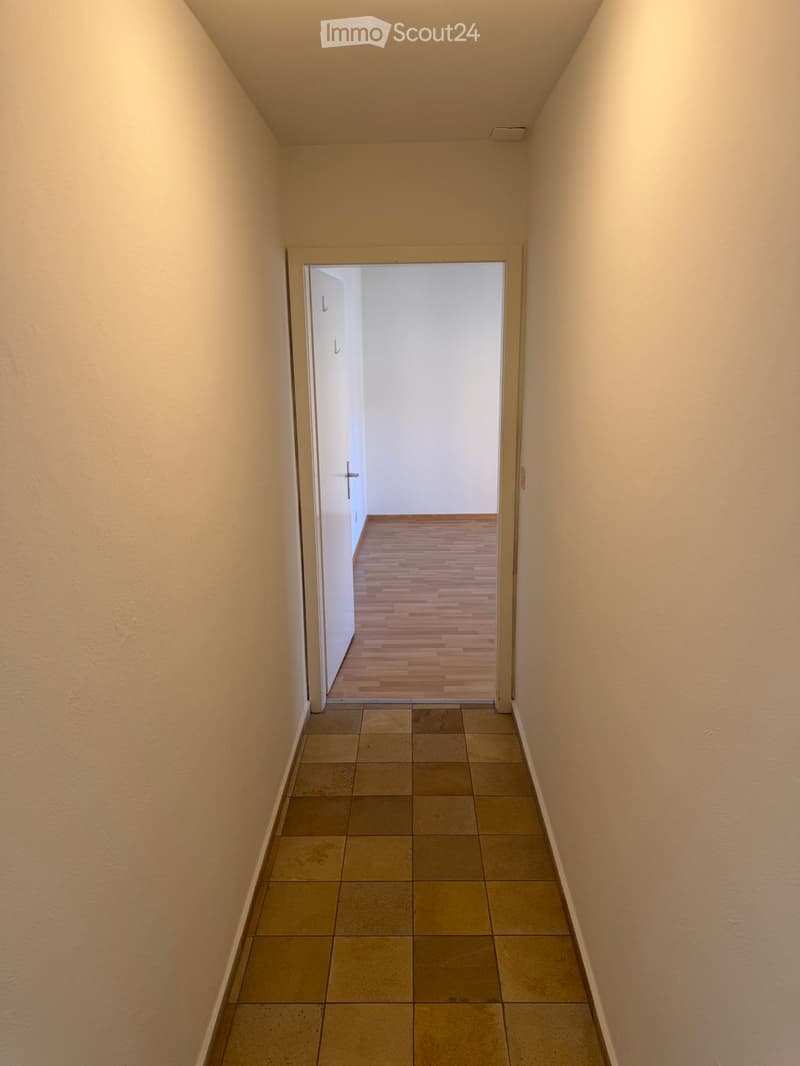 Empty hallway with tiled floor and wooden flooring visible through an open door at the end.