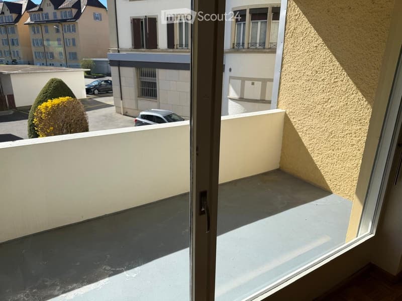 Balcony with a view of a residential area, featuring a low wall, concrete floor, and surrounding buildings.