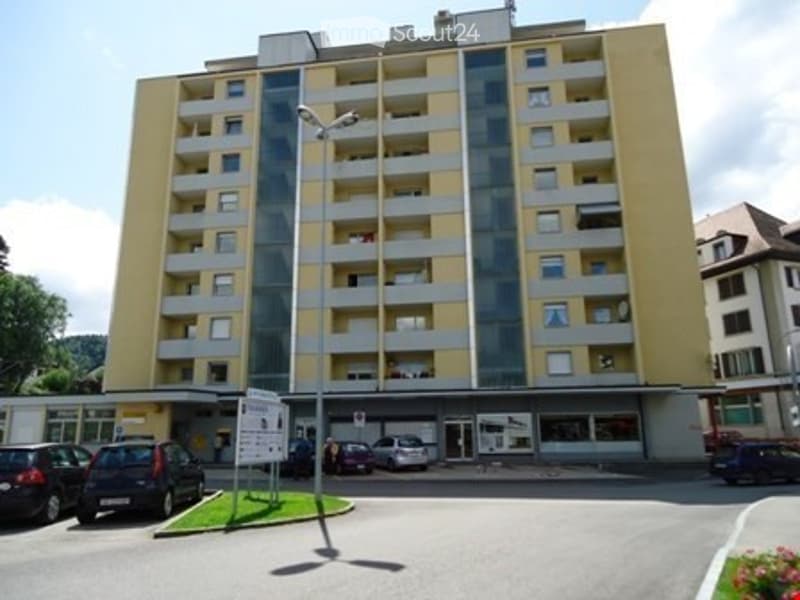 Multi-story residential building with balconies, parking area, and street signage.