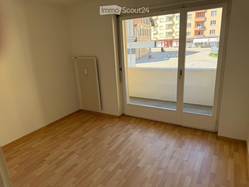 Empty room with wooden flooring, white walls, and a large sliding glass door leading to a street view.