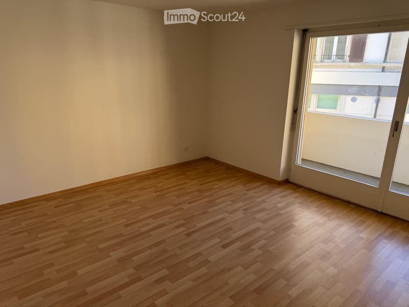 Empty room with wooden flooring and large window offering a view of the street.