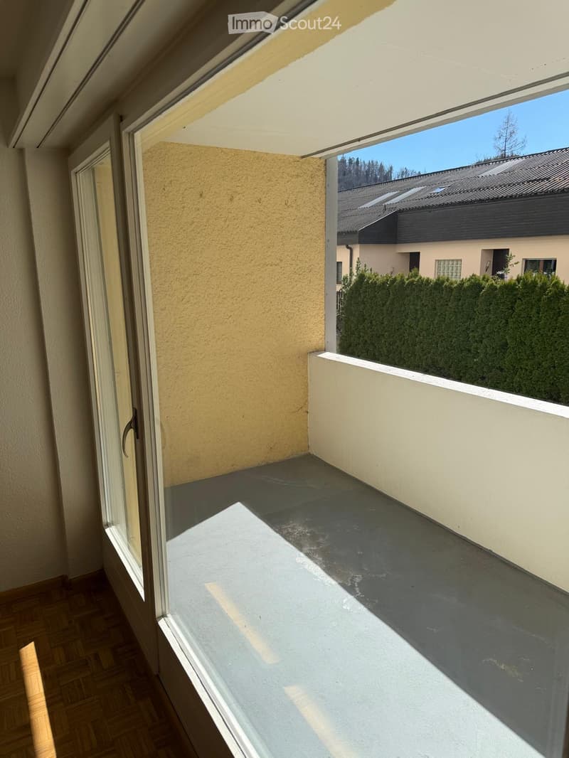 Balcony with concrete floor, white railing, and view of neighboring houses and greenery.