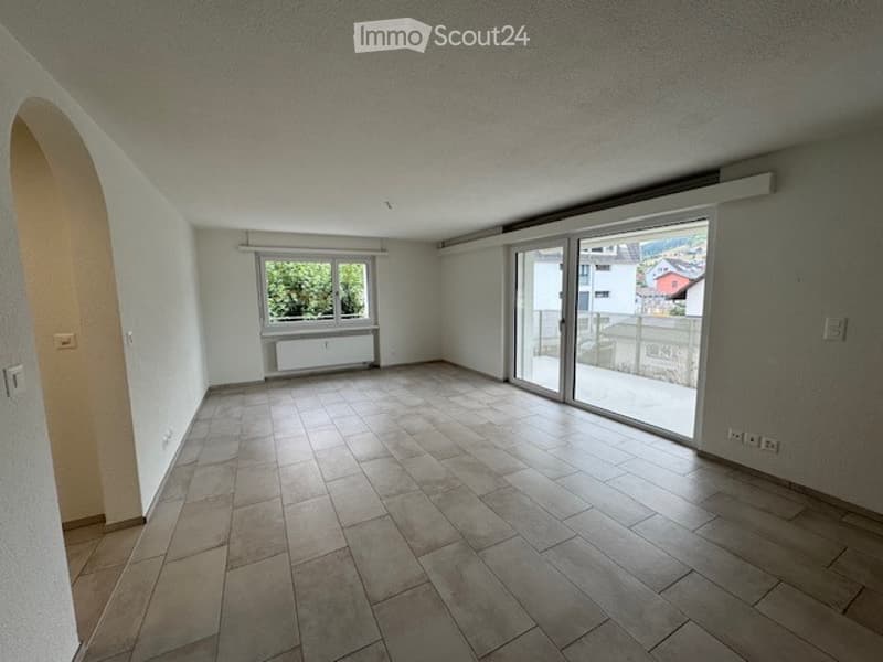 Empty room with tiled floor, large window, sliding glass door leading to a balcony, and white walls.