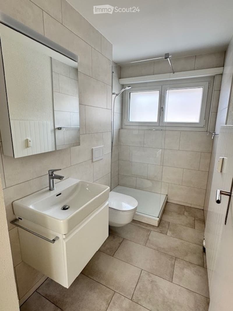Modern bathroom with beige tiles, a white sink with a mirror cabinet, a toilet, and a glass-enclosed shower area.