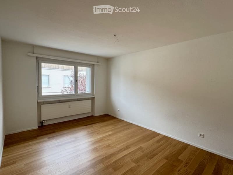 Empty room with wooden flooring, white walls, and a window with a radiator below it. No furniture or equipment present.