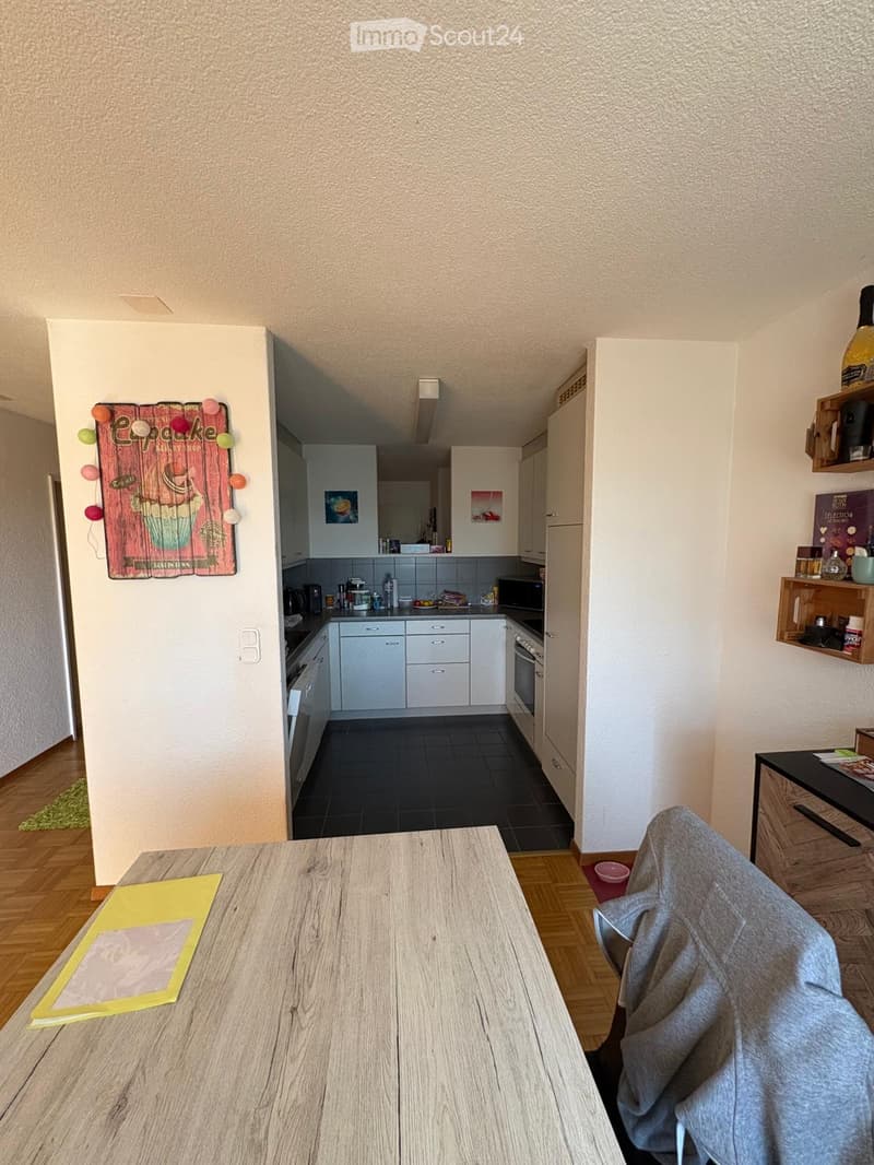A modern, well-lit kitchen and dining area with white cabinets, a wooden dining table, and various appliances.