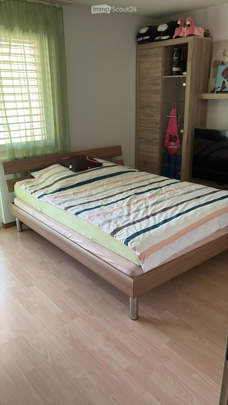 A modern bedroom with a wooden bed, striped bedding, a wardrobe with shelves, and a window with green curtains.