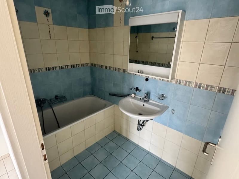 Bathroom with blue and beige tiles, a bathtub, a sink with a mirror cabinet, and a towel rack.