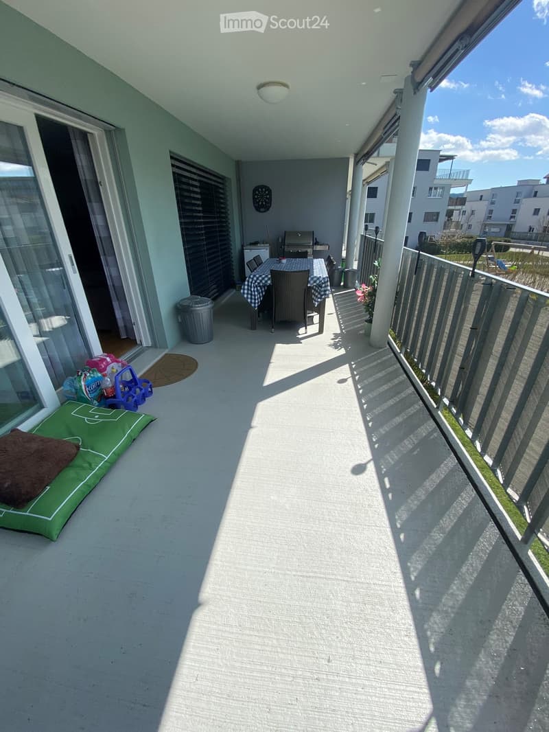 Enclosed balcony with railings, outdoor table and chairs, potted plants, a mat, and a trash can, along with some household items
