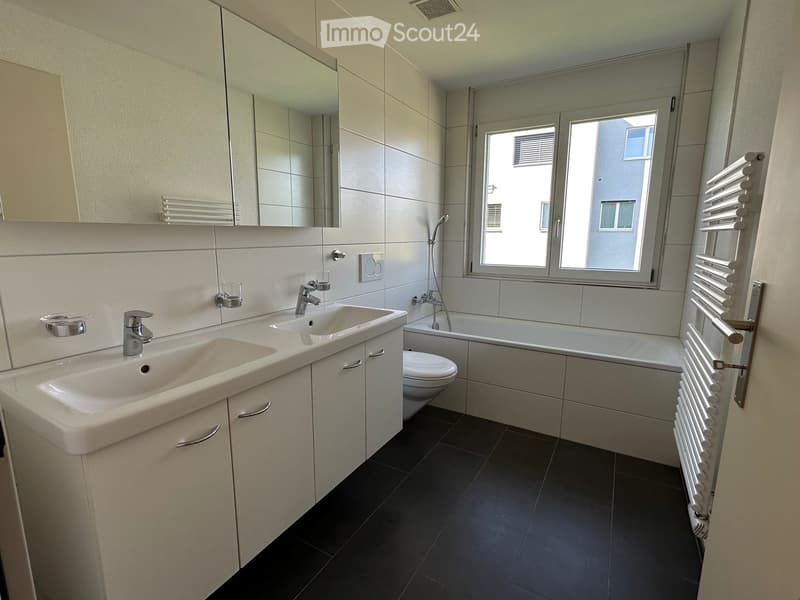 Modern bathroom with white tiles, double sink, mirror, shower, toilet, and bathtub.