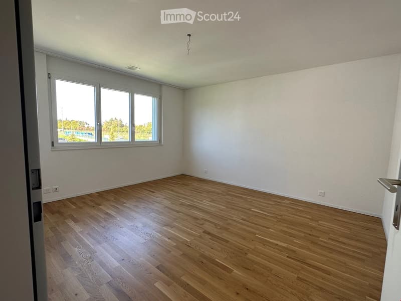 Empty living space, hardwood floor, white walls, large windows, view of outdoor area