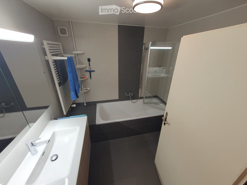 Modern bathroom with a white sink, bathtub, and glass-enclosed shower stall. Features a towel rack with blue towels and a sleek, contemporary design.