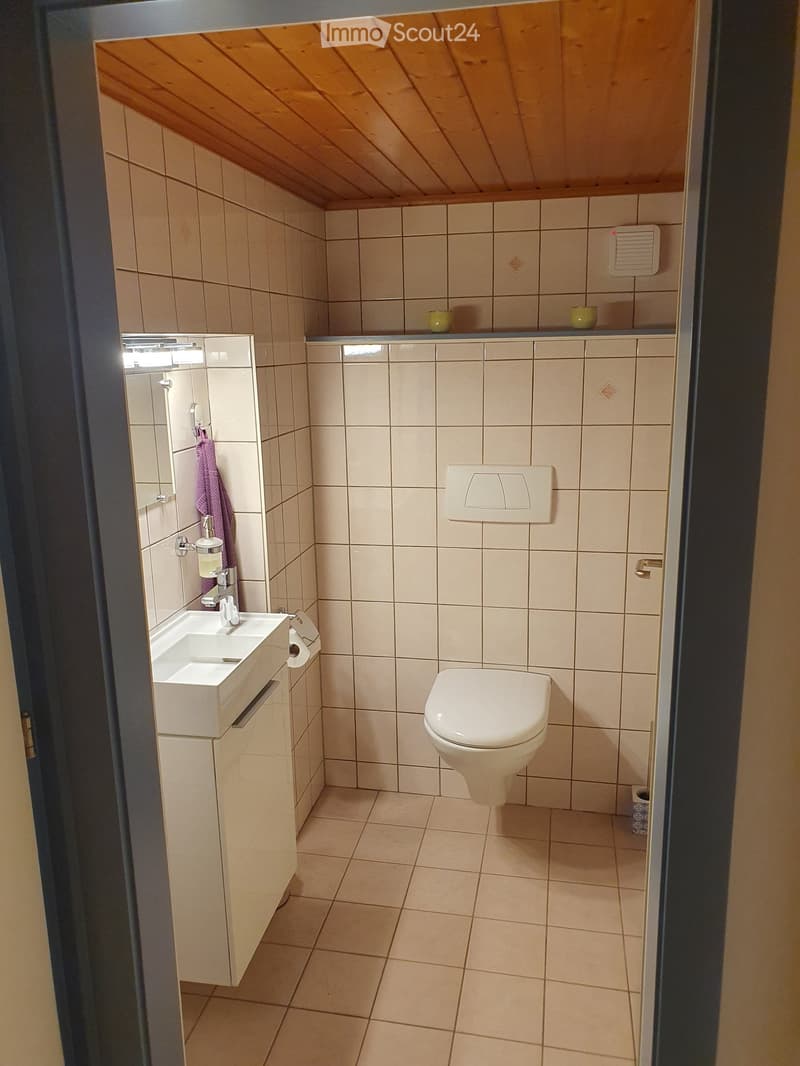 Modern bathroom with beige tiles, a white sink, a toilet, a mirror, and a towel hanging on the wall.