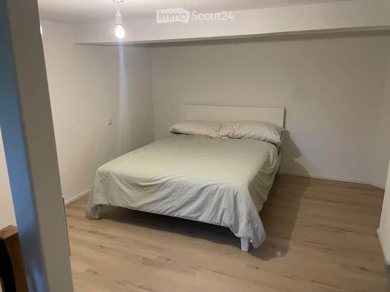 A small bedroom with a single bed, headboard, and light-colored bedding on a wooden floor.