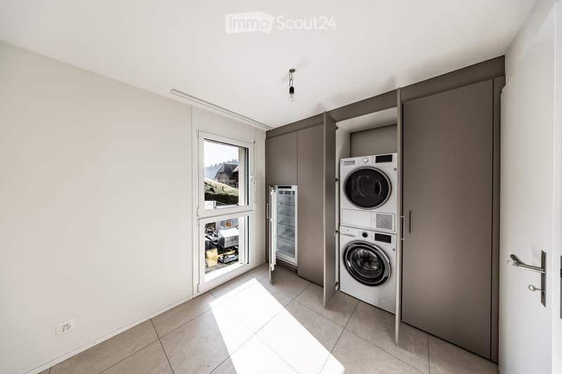 Modern, minimalist laundry room with a washing machine, refrigerator, and built-in storage cabinets.