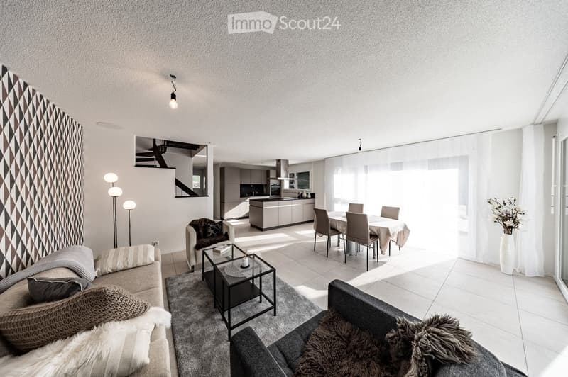 Open-plan living and dining area with modern furniture, including a sofa, coffee table, dining table, and chairs. The space features large windows, a sleek kitchen area, and decorative elements like a vase with flowers and a floor lamp.