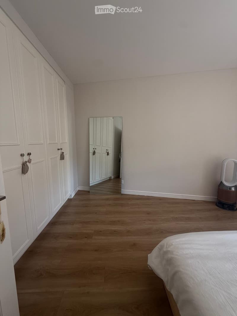 Spacious bedroom with wooden flooring, large bed, built-in wardrobes, and a mirror reflecting part of the room.
