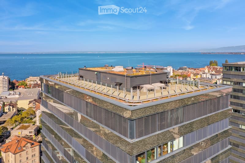Modern multi-story building with a rooftop terrace overlooking a body of water and cityscape.