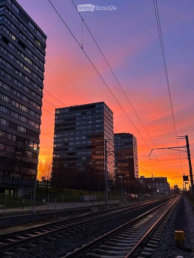 Modern high-rise buildings in an urban setting during sunset, with train tracks in the foreground.
