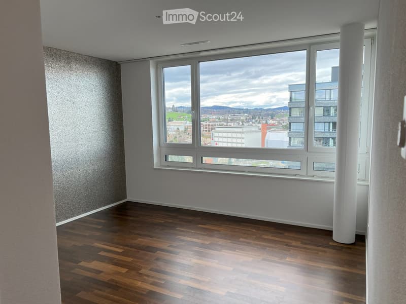 Empty room with wooden flooring, large windows, and a view of the city and mountains.