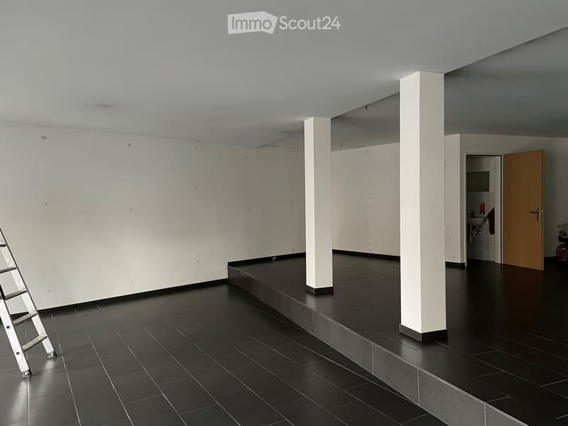 Empty room with dark tiled flooring, white walls, and a small adjacent bathroom area visible through an open doorway.