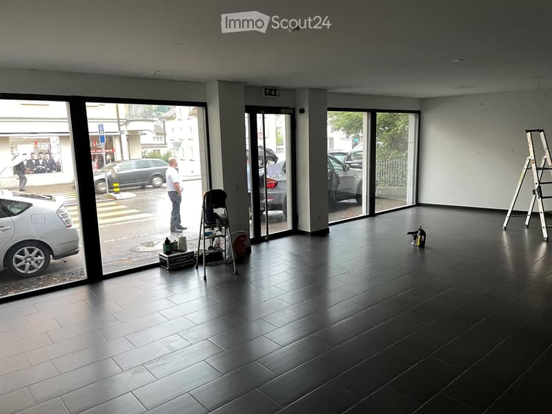 Empty room with dark tiled flooring, large glass windows, and a few cleaning supplies near the entrance.