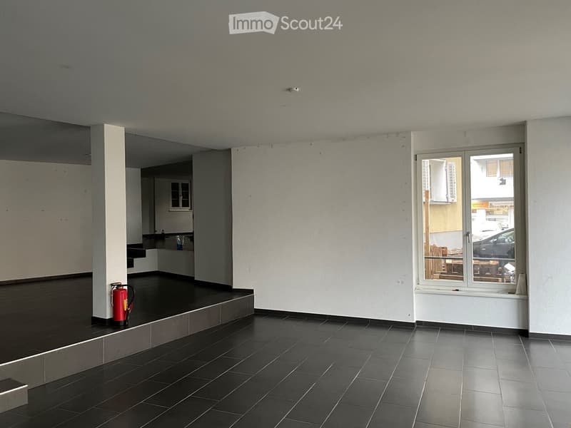 Empty room with dark tiled floor, white walls, and a large window showing a view of another room. A red fire extinguisher is placed near the wall.
