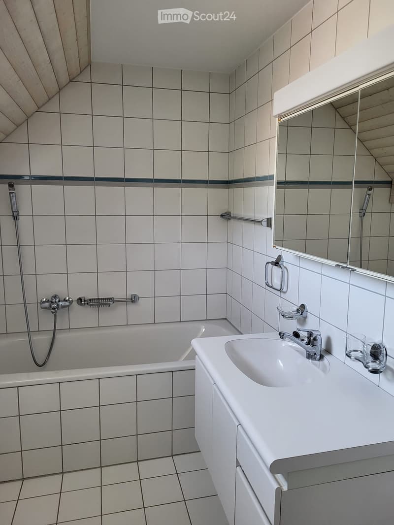 Modern bathroom with white tiles, a bathtub, a sink with a faucet, a mirror, and two cups on the counter.