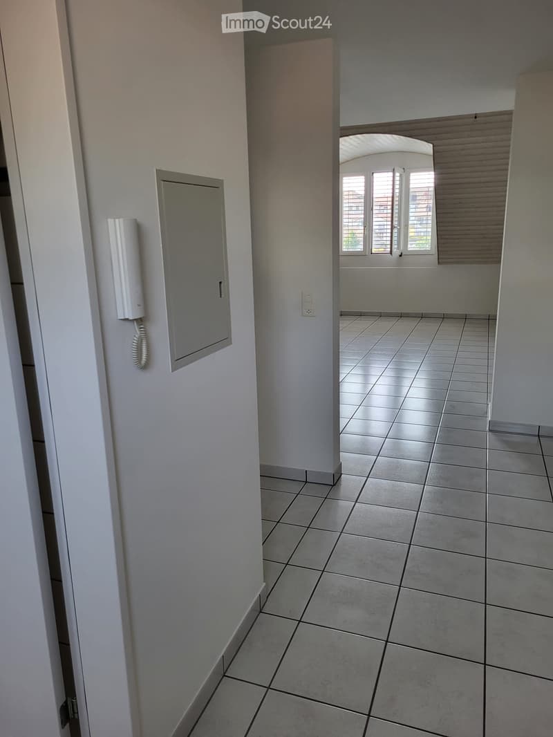 Empty hallway with tiled floor, white walls, and a window with blinds at the end.