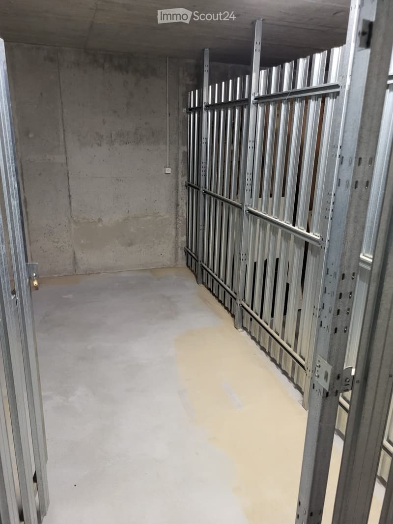 Empty corridor with concrete walls and floor, metal framing on one side, and a visible electrical outlet on the wall.