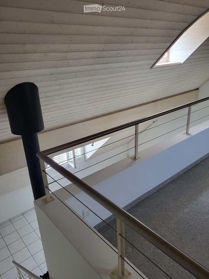 Modern hallway with wooden ceiling, glass railing, and tiled floor. Features a black cylindrical object on the left and a small window at the top right.
