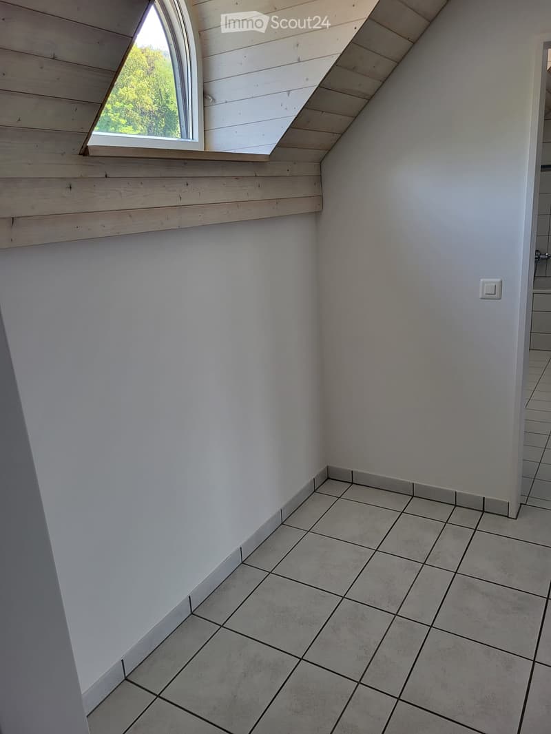 Empty room with white walls, tiled floor, and a skylight window showing greenery outside.