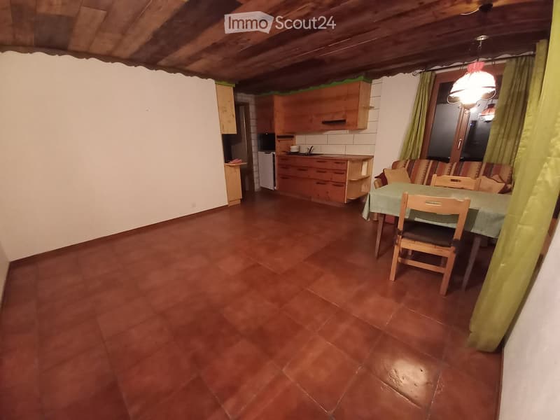 A cozy, rustic living and dining area with wooden beams, terracotta tiles, and a mix of kitchen and living space.
