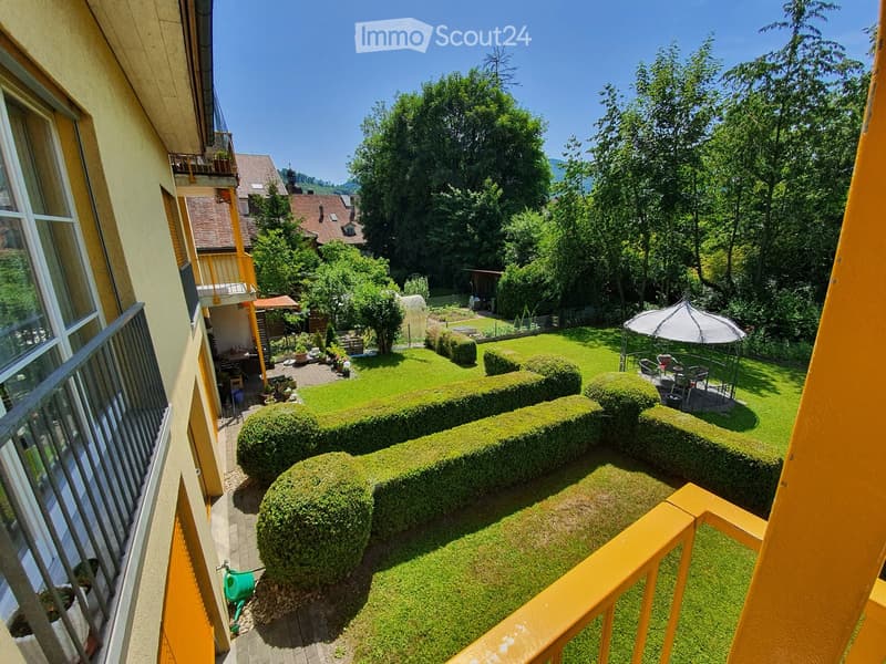 Well-maintained garden with neatly trimmed hedges, a small patio area with outdoor furniture, and a view of neighboring houses and trees.
