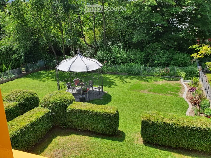 Well-maintained garden with a gazebo, neatly trimmed hedges, and a small seating area with chairs and a table.
