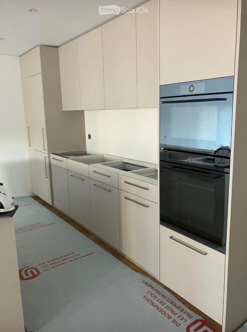 Modern kitchen with white cabinets, stainless steel sink, and built-in oven. Light-colored flooring and sleek design.
