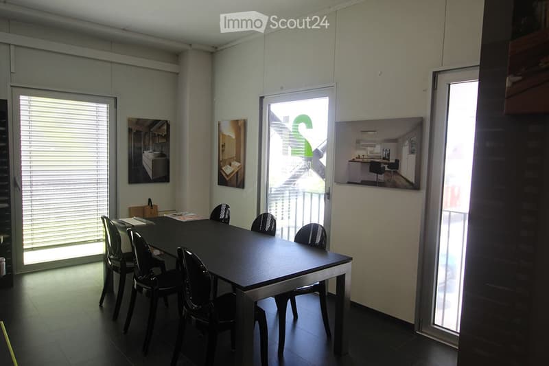 A modern, minimalist meeting room with a black table and six black chairs, large windows with blinds, and artwork on the walls.